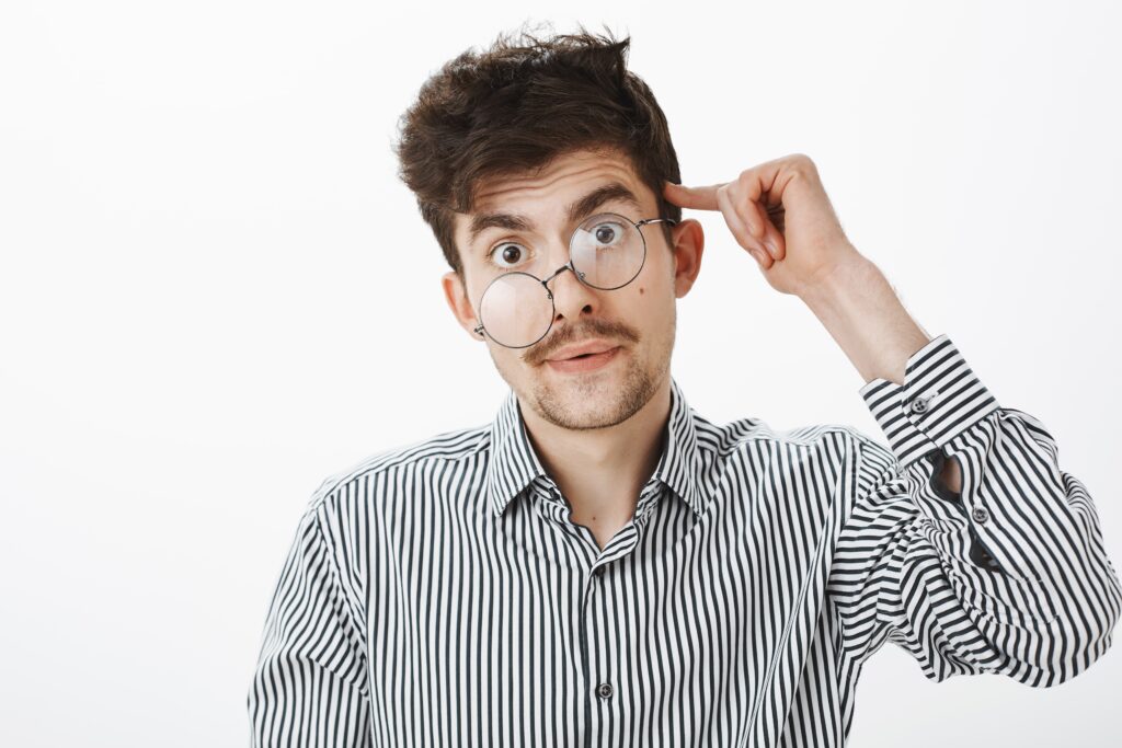 Confused young man in striped shirt with broken glasses pointing at his head